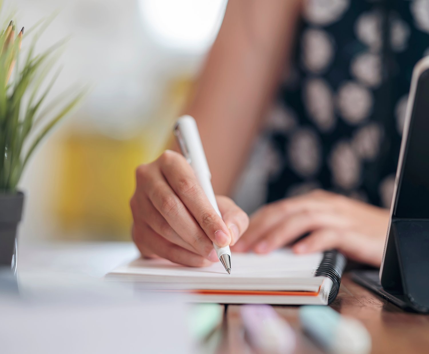 Close-up of a hand writing on a document beside a laptop