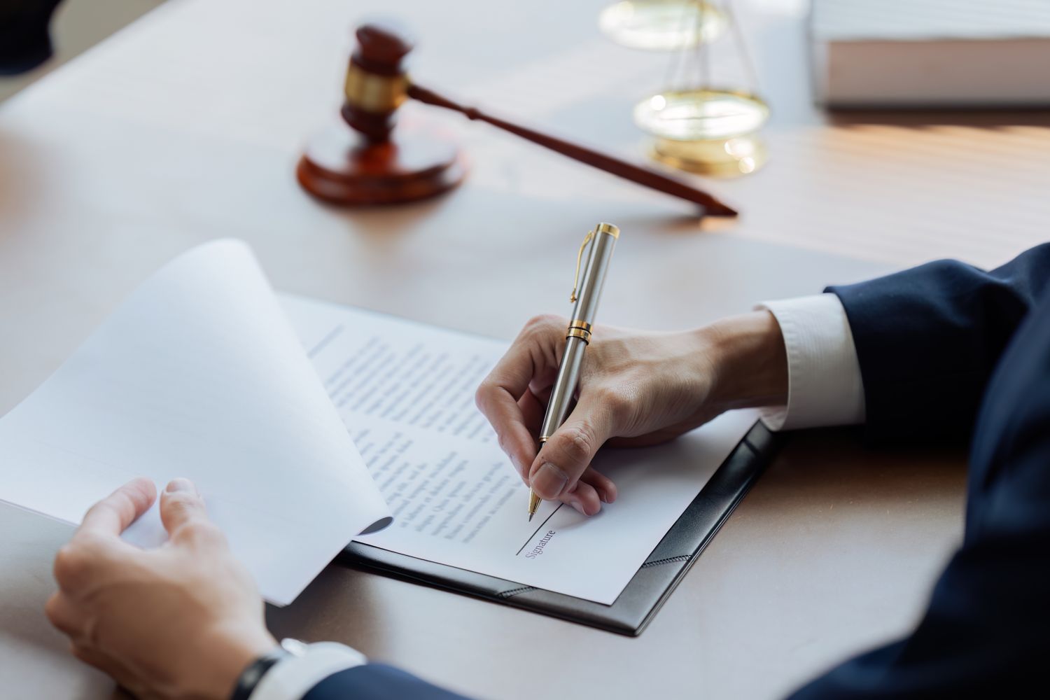 Hand signing a legal document with a fountain pen, gavel nearby