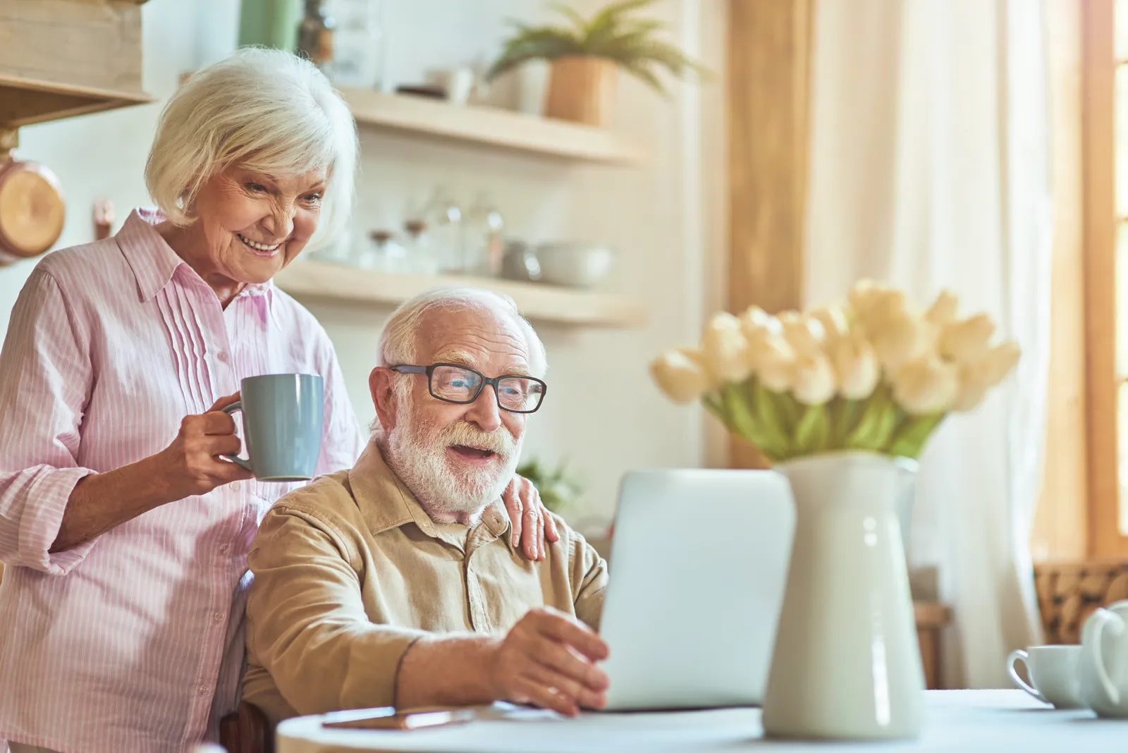 An older couple sitting together at their kitchen table reviewing paperwork on a laptop